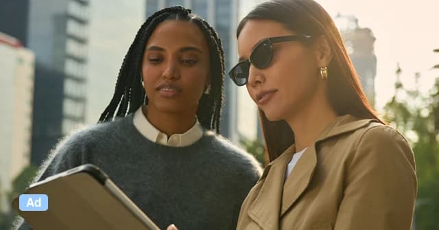 Two colleagues reviewing a tablet together on a city street, with an Ad badge in the corner